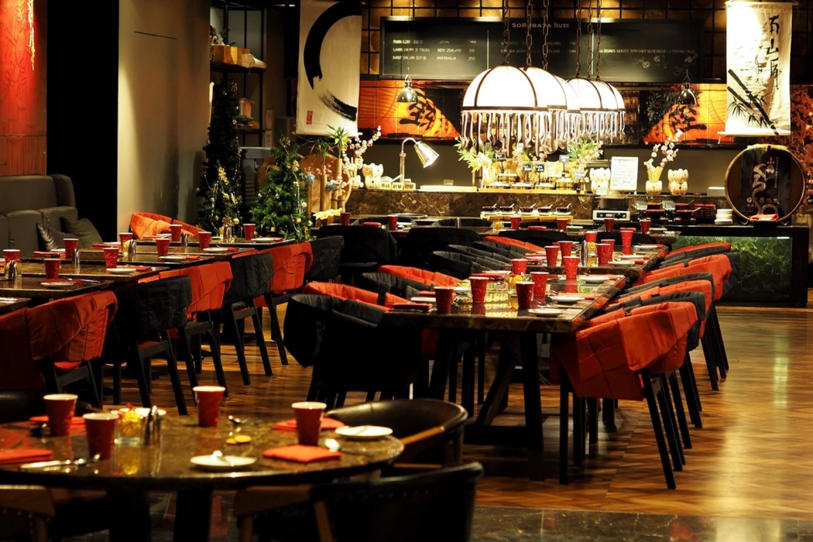 A warm, busy-looking restaurant dining room with long rows of set tables